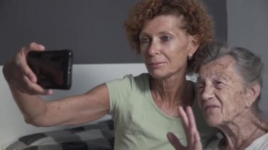 Olgun kız, huzurevindeki yaşlı anneyi ziyaret ediyor. Yaşlı bir kadın yatak odasında kızıyla kucaklaşır ve akıllı telefondan video görüşmesi yapar. Koronavirüs sırasında yaşlıları tecrit etmek