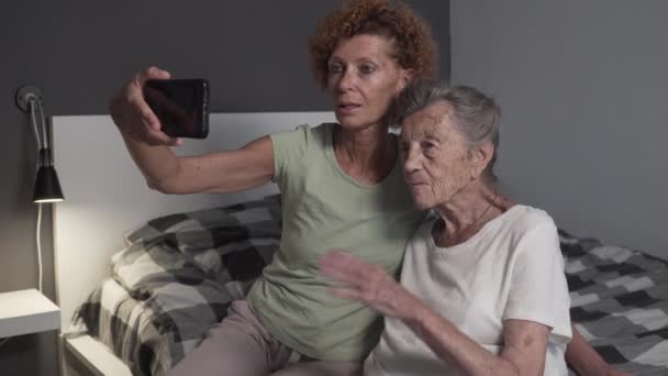 Mujer mayor y la hija de videoconferencia en el teléfono inteligente en casa. Tecnología, concepto de personas mayores. Ancianos abuela de pelo gris y hembra adulta haciendo videollamada en el hogar de ancianos — Vídeos de Stock