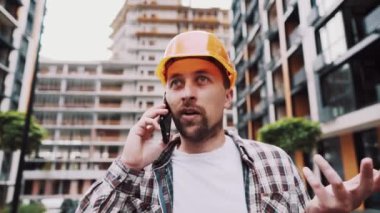 Turuncu şapkalı kızgın erkek mimar inşaat alanında telefonla konuşuyor. Ekose gömlekli bir inşaatçı cep telefonuyla pazarlık etmekten rahatsız olur. Çığlık atan stresli mimari tasarımcı