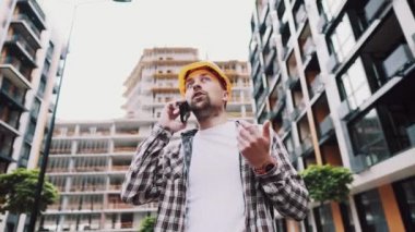 Turuncu şapkalı kızgın erkek mimar inşaat alanında telefonla konuşuyor. Ekose gömlekli bir inşaatçı cep telefonuyla pazarlık etmekten rahatsız olur. Çığlık atan stresli mimari tasarımcı
