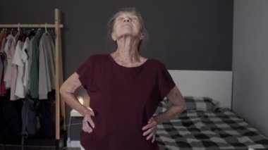 Aktif kıdemli kadın evde egzersiz yapıyor. Olgun beyaz kadın yatak odasında egzersiz yapıyor. Gelişmiş sağlık için uzanıyor. 90 yaşındaki büyükanne koronavirüs salgını karantinasında ısınıyor.