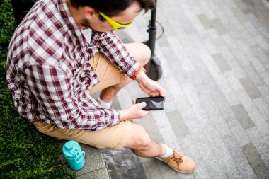 Beyaz adam şehirde elektrikli scooter 'ın yanındaki bankta otururken internet ve cep telefonuyla modern teknolojiler kullanıyor. Ekoloji ve çevre dostu şehir taşımacılığı.