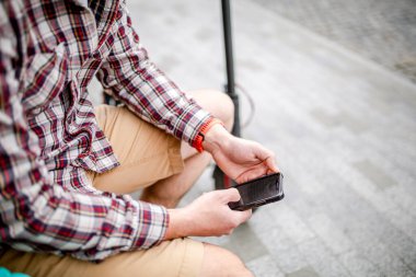 Modern ekolojik temiz taşıma teması. Kentte elektrikli scooter 'a bindikten sonra elinde akıllı bir telefonla bankta dinlenen bir adam. Motosikletli bir erkek mesajları kontrol ediyor.