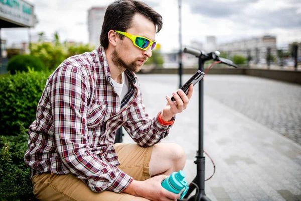 캅카스 남성은 스쿠터 도시의 벤치에 스마트폰으로 현대적 기술의 인터넷과 통신을 — 스톡 사진