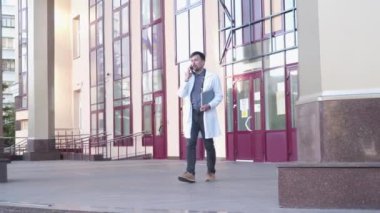 Tıbbi sağlık hizmeti profesyonel teması. Beyaz laboratuvar önlüklü genç doktor hastayla cep telefonuyla konuşurken hastane binasını terk ediyor. Tıp fakültesi öğrencisi giriş dışında akıllı telefon kullanıyor.