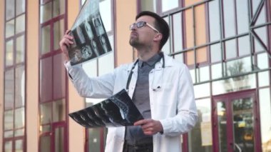 Tıp ve sağlık teması. Tıp öğrencisi, üniversite girişinin dışındaki akciğerlerin tomografisini inceliyor. Coronavirus hastasının röntgenlerini inceleyen genç bir tıp çalışanı. Doktor MRI taramasını analiz eder.