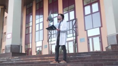 Steteskop giyen doktor dışarıda hastane girişinin yanında röntgen görüntülerini analiz ediyor. Genç sağlık uzmanı, internet radyologu COVID 19 salgını sırasında MRI-ray ciğerlerini muayene ediyor.