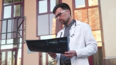 Tıp ve sağlık teması. Tıp öğrencisi, üniversite girişinin dışındaki akciğerlerin tomografisini inceliyor. Coronavirus hastasının röntgenlerini inceleyen genç bir tıp çalışanı. Doktor MRI taramasını analiz eder.