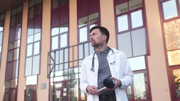 Młody lekarz, stażysta w białym fartuchu laboratoryjnym, stoi przy głównym wejściu do szpitala z prześwietleniem lub tomografią komputerową. Radiolog badający tomografię na zewnątrz. Zapalenie płuc, koncepcja wirusa korony — Wideo stockowe
