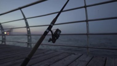 Akşamları, deniz kıyısındaki ahşap bir iskelede olta ve olta. Balık kavramı. 4K çözünürlük, elde taşınan video kaydı, canlı kamera