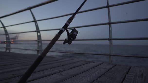 Primer plano de una caña de pescar con un carrete sin personas en un muelle de madera cerca del mar negro en Odesa. Resolución 4K, grabación de vídeo desde un trípode — Vídeo de stock