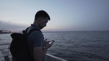 Kafkasyalı genç bir adam deniz akşamına yakın bir rıhtımda dinlenirken akıllı telefondan fotoğraf çekiyor. Erkek Karadeniz 'de günbatımının fotoğrafını çekiyor. Cep telefonu kamerasıyla deniz kenarındaki akşam manzarası