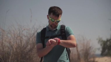 Yürüyüş sırasında cep telefonunu kontrol eden bir adam. Genç bir erkek, deniz boyunca bir tepenin üzerinde yürüyüş yaparken cep telefonu GPS 'ini kullanıyor. Akıllı telefon uygulaması haritasında gezgin görünümü rotası