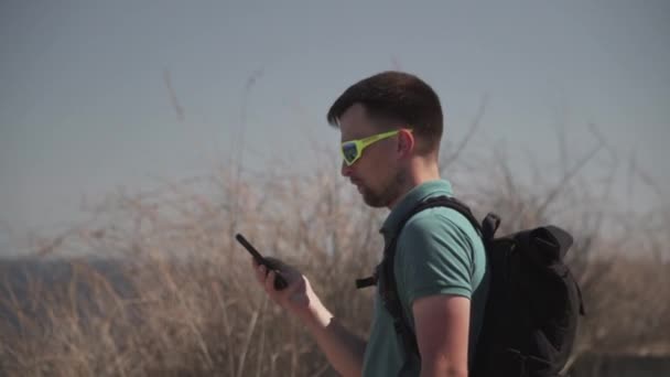 Caucasian man walks along trail on hill along sea, one-day hiker uses the Internet and smartphone app to navigate. Male builds a route in phone using satellites gps for orientation and geolocation — Stock Video