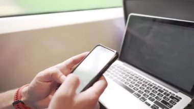 Telefondaki adam dizüstü bilgisayarla mesaj atıyor. Koronavirüs salgını sırasında banliyö treninde maske takıyor. Tema trenle seyahat, COVID 19 sırasında yeni kurallar. Erkek trende akıllı telefon ve dizüstü bilgisayar kullanır