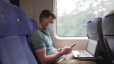 Tema bir gezide çalışmak. Kafkas asıllı genç bir erkek, pencerenin yanında trende otururken akıllı telefonuyla mesaj atıyor ve yüzünde koruyucu bir tıbbi maske takarak dizüstü bilgisayarla çalışıyor.