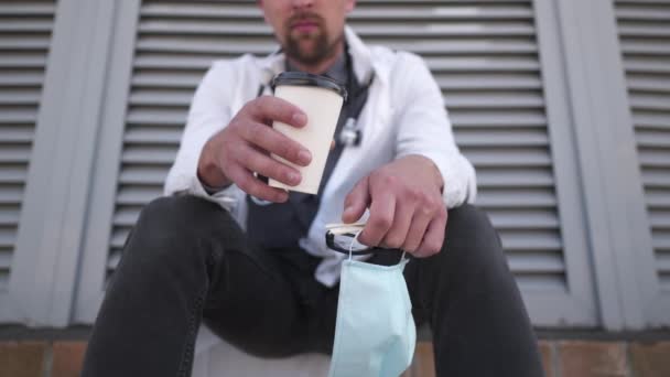 Manos de cerca con café taza y máscara médica protectora relajante después de la recuperación de los pacientes y el trabajo duro. Trabajador de la salud se siente cansado después de proteger y luchar covid 19 con bebida caliente, energizante — Vídeos de Stock