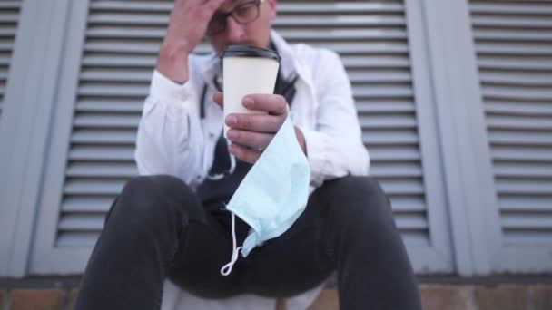 Close-up van de hand met kopje koffie en beschermende medische masker. Moe, uitgeput arts in medische witte jas tijdens de koffiepauze buiten ziekenhuis in de ochtend. COVID-19, coronaviruspandemie — Stockvideo