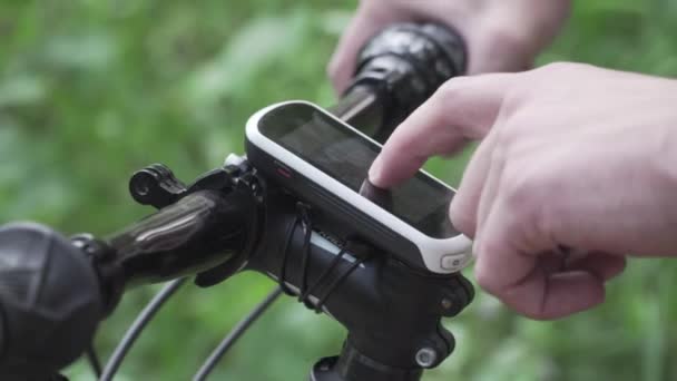 Adam gidona sabitlenmiş akıllı bisiklet bilgisayarı kullanıyor, bisikletçi ormanda bisiklet sürerken GPS koordinatlarını bulmak için navigatör kullanıyor. Çevrimdışı turizm ve seyahat haritaları içeren bir bisiklet bilgisayarı — Stok video