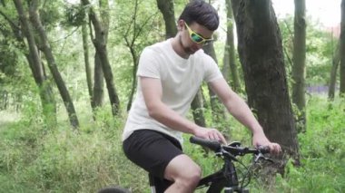 Dağ bisikleti süren spor giyimli bir erkek bisiklet bilgisayarında gezinmek için bir cihaz kullanıyor. Ormanda spor yapan bir adam, tahta üzerinde bisiklete biniyor ve elinde GPS navigatörü tutuyor. Guy uygulama ekran haritasına dokun