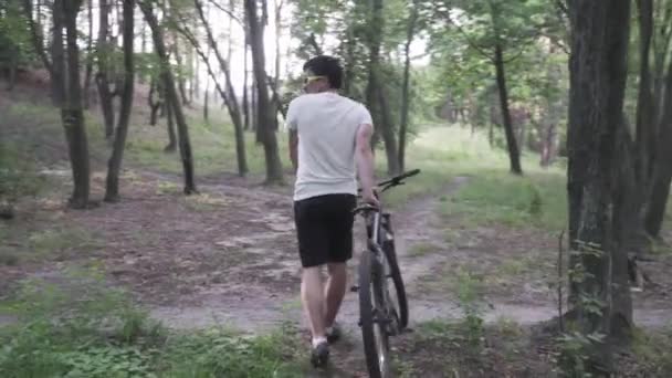 Beyaz adam orman yolunda siyah dağ bisikleti sürüyor. Açık havada dağ bisikleti süren bir erkek bisikletçi. Hareket, egzersiz. Sporcu dağ bisikletçisi orman yolu boyunca bisiklet sürer. Etkin yaşam biçimi — Stok video