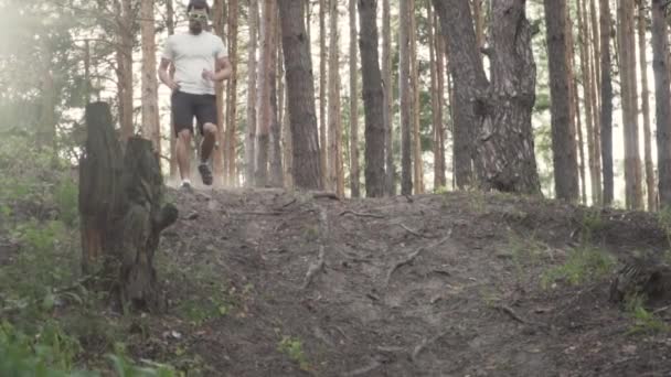 Wolny ruch Biały mężczyzna atleta biegnie na wzgórzu w lesie o zachodzie słońca. Męski biegacz uprawia jogging biegowy po górskiej szorstkiej drodze terenowej. Trasa dla początkujących sportowców — Wideo stockowe