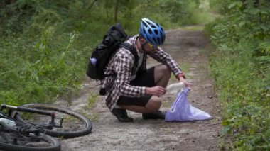 Sporcu gönüllü, dağ bisikleti eğitimi sırasında ulusal bir parkta çöp torbasında çöp topluyor. CSR aktiviteleri, çevre sorunları, kirlilik ve plastik geri dönüşümü. Orman temizliği