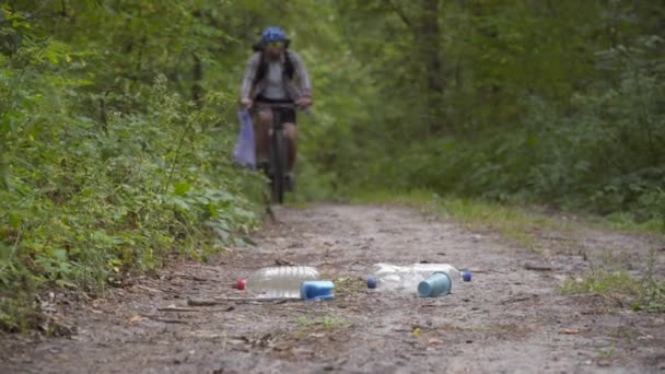 Ökologie, Umweltverschmutzung, Müll und weggeworfenes Plastik. Radfahrer sammelt beim Radeln im Wald Müll in Tüten ein Ehrenamtlicher Sportler schält Plastikflaschen im Park ab und nimmt sie zum Recycling mit — Stockvideo