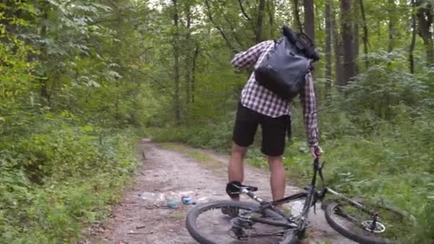 Człowiek jeździ rowerem po lesie, zbierając śmieci. Modne programy sportowe, które pomagają zachować środowisko. Zanieczyszczenia. Problem ekologiczny. Świadomość zakazu tworzyw sztucznych, koncepcja krajowego dnia sprzątania — Wideo stockowe