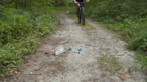 Ecology theme, pollution, rubbish and plastic discarded. Cyclist picks up trash in bag during cycling in forest. Athlete volunteer peels off plastic bottles in park and takes them away for recycling — Stock Video