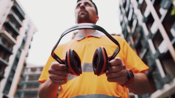 Человек с защитным оборудованием для слуха. Работник, носящий шумоподавляющее защитное ухо или наушники. Строитель надевает защитные уши с наушниками. Безопасность во время работы — стоковое видео