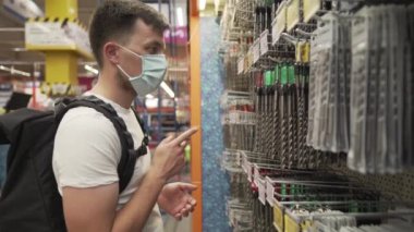 Tıbbi maskeli beyaz adam hırdavatçıdaki inşaat malzemeleri için matkap ucu seçiyor. Covid 19 salgını sırasında süpermarket inşaatında sondaj makinesi olarak kullanılan erkek tercihi metal matkabı.