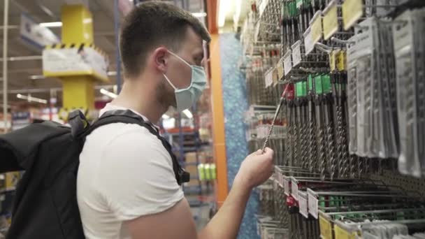 Employee choosing concrete drill bit in tool store wearing a protective mask on his face during the coronavirus epidemic. buyer in a hardware store selects a product on covid 19. Kit for repair work — Stock Video