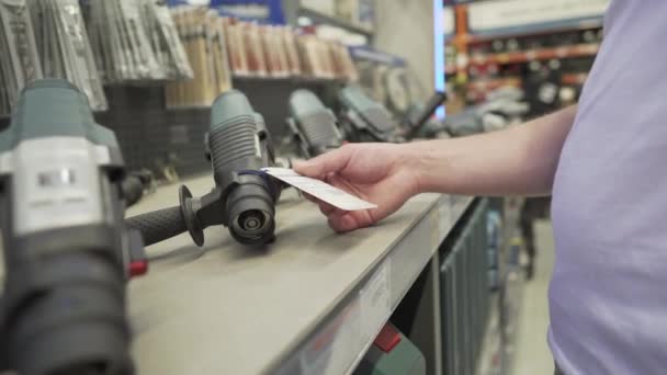 Άντρας αγοραστής επιλέγει ένα ηλεκτρικό χέρι εργαλείο στο τμήμα ενός σούπερ μάρκετ κτίριο φορώντας μια προστατευτική ιατρική μάσκα. Ένας άνδρας επισκευαστής σε ένα κατάστημα υλικού αγοράζει ένα εργαλείο κατά τη διάρκεια του covid 19 — Αρχείο Βίντεο
