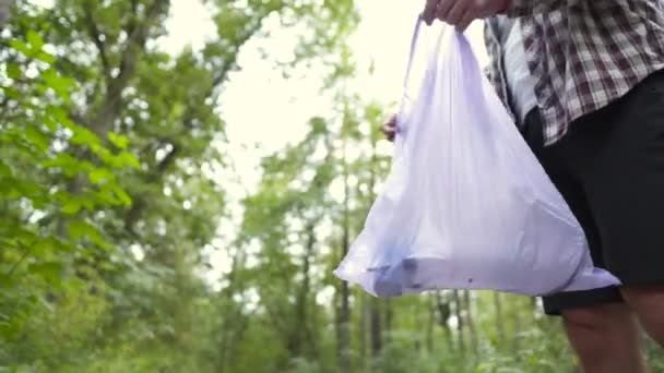 Un hombre malo tira basura de una bolsa de basura plástica en el bosque. El intruso macho deja basura y se aleja. Contaminación y problemas ecológicos, reciclaje de plásticos, contaminación de la naturaleza — Vídeo de stock