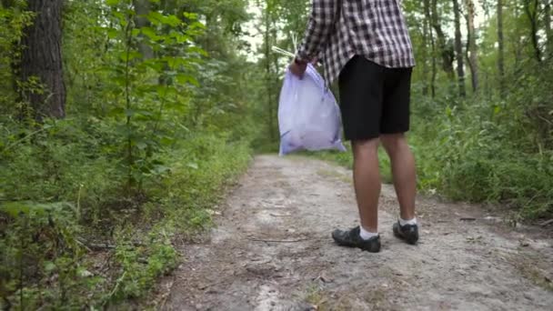 Egy fiatalember szemetet dobál a műanyag zacskóból a földön. Környezetszennyezés. Globális felmelegedés. A férfi kidobja a szemetet az erdőben. Ökológiai probléma. Dobd ki a szemetet! Szennyezett talaj — Stock videók