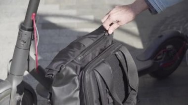 Modern akıllı cihazlar ve aletler günlük hayatta şehirli kişide. Yetişkin bir kadın elektrikli scooter 'ın yanındaki bankta dinleniyor ve portatif şarj aletinden şarj oluyor.