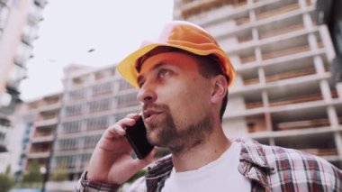 Mühendis telefonda konuşuyor. İnşaat alanında telefonu kullanan bir mimar. Foreman 'ın telefon kontrol işlemleri. İnşaat sektöründe inşaat işçisi iletişimi. Profesyonel telefon binası