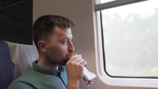 白人男性旅行者在靠窗座位的高速列车上旅行，吃快餐三明治卷。铁路车辆内部。一个人坐火车和吃零食。垃圾食品走了 — 图库视频影像