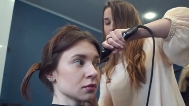 Краса, концепція зачіски, щаслива молода жінка і перукарня з заліза для волосся роблять зачіску в перукарні. Жінка має волосся стилізований перукар. Згладжує кьорлінг волосся. Стиліст Використовуючи інструмент для моделювання — стокове відео