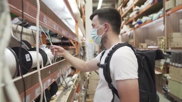 Acquirente maschio scegliendo corda materiale da costruzione in ferramenta. Bel caposquadra che sceglie le merci nel negozio di costruzione. Hardware store client fare un po 'di shopping per l'uso del progetto protettivo covid 19 maschera — Video Stock