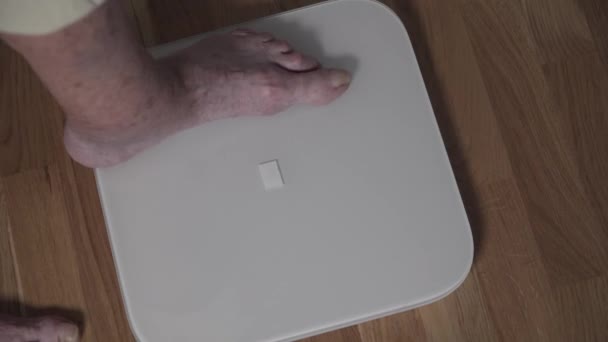 Close-up of leg of an old elderly woman getting on the electronic floor scale. A senior female with sore crooked toes and scary nails is weighed on a home scale in the living room. Healthy retirement — Stock Video