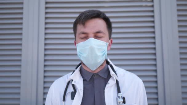 Zmęczony smutny biały mężczyzna lekarz zdejmuje maskę medyczną, odpoczywając opierając się o ścianę. Mężczyzna odpoczywa po ciężkiej pracy. Stracił życie podczas wideoklipu 19. Trudny dzień rozczarowany lekarz. Zbliżenie twarzy — Wideo stockowe