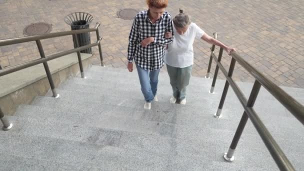 Proporcionar ayuda y apoyo a las personas mayores. Abuela, paciente. Mujer ayudando a la abuela a subir escaleras. Mujer mayor con cuidador domiciliario. Enfermera ayudando a apoyar, ayudando a la mujer mayor a subir a las escaleras — Vídeo de stock