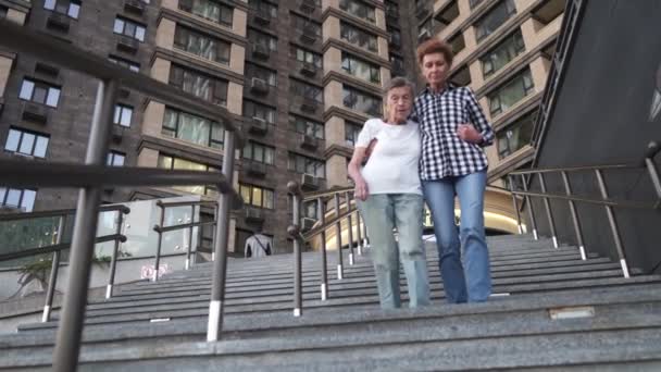 Home carer helping disabled woman getting down the stairs. Nurse helping a senior woman walk on stairs. Caregiver helping retired people go on stairs outside. Providing help and support for elderly — Stock Video