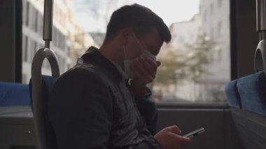 Tıbbi maskeli hasta adam Avrupa 'da toplu taşıma araçlarında hapşırıyor, akıllı telefon kullanıyor. İşe gidip gelirken virüs ve enfeksiyona karşı koruyucu yüz maskesi. Salgın önleme ve hijyen kavramı.