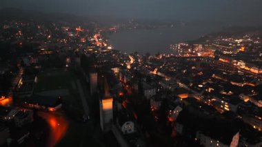 Musegg Wall ve dokuz kulesi geceleri İsviçre 'nin Lucerne kentindeki parlayan şehre bakıyor. Lucerne 'in ortaçağ savunması. Museggmauer Luzern und ihre neun Tuerme Luftaufnahme bei Nacht.