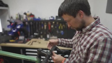 Bisikletli tamirci atölyesindeki çakıl bisikletinin gidon bandına sarılmış. Bisiklet teknisyeni kaseti dikkatlice gidonun etrafına sarar ve atölyede bakım yapar..