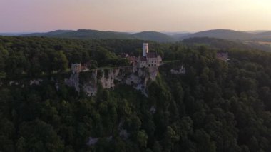 Lichtenstein Kalesi 'nin hava günbatımı görüntüleri. Honau, Almanya' nın yukarısındaki Albtrauf sırtına tünemiş. Bu romantik dağ kalesi, orman ve sarp kayalıklarla çevrili ılık bir ışıkla parıldıyor..