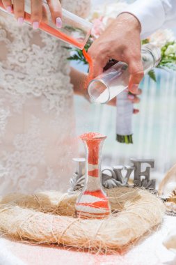 Gelin ve damat kristal vazoya renkli kumlar döküyor. Sembolik deniz dekoru merasimi sırasında okyanusun önündeki kumlu kumsalda evlilik birleşme töreni sırasında kapatılıyor. 